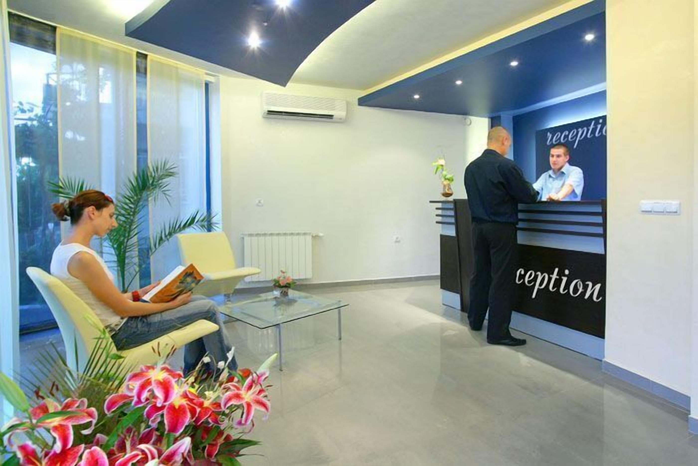 A reception area with a reception desk, a waiting area with a glass table and chairs, and a large window with blinds.