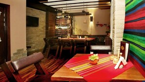 Un comedor acogedor con una mesa de madera, sillas y un camino de mesa rojo. Hay una zona de bar con estantes llenos de botellas y un televisor al fondo.