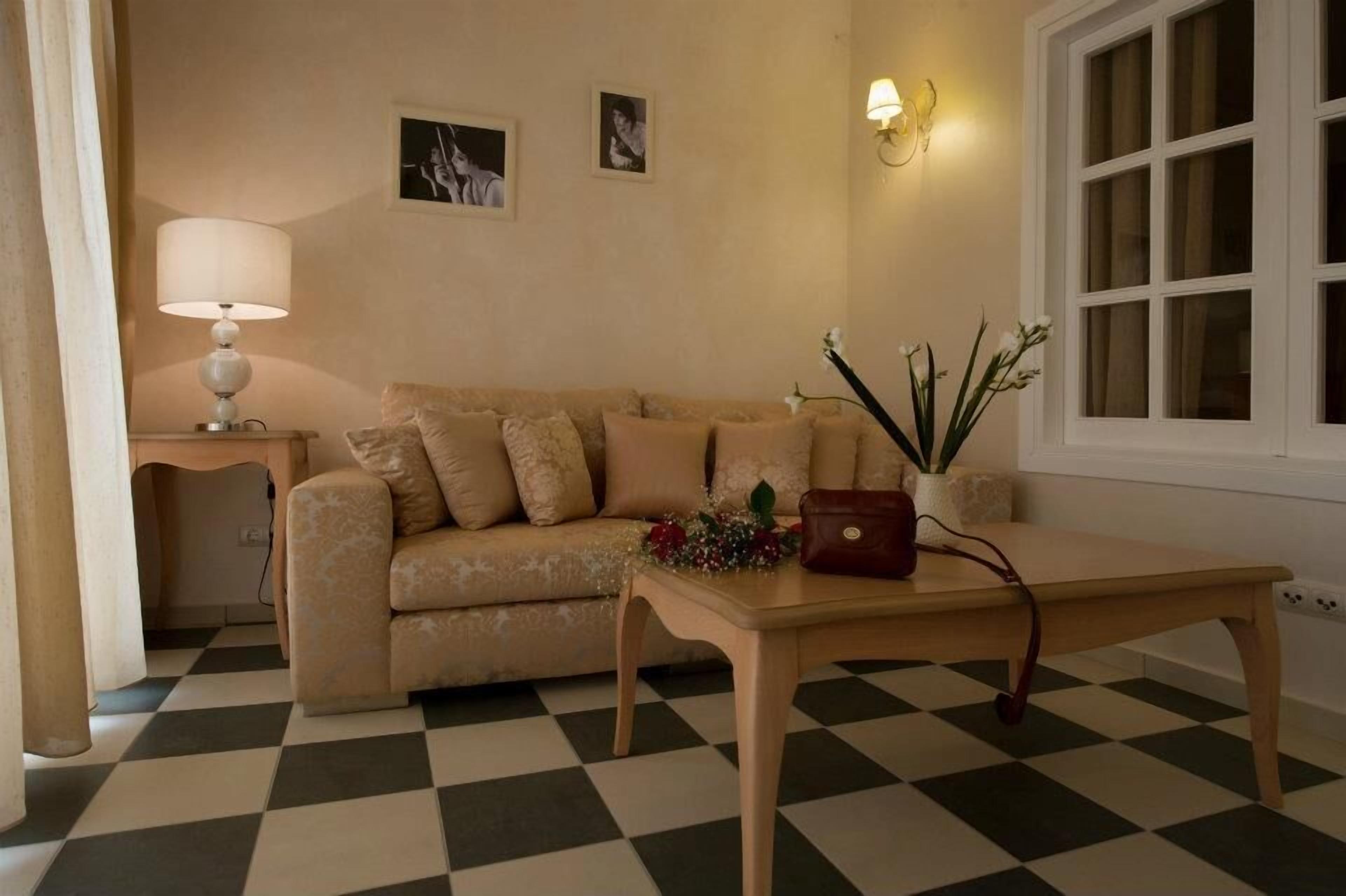 A living room with a checkered floor, a sofa, a table with a vase and flowers, a lamp, and a wall-mounted light fixture.