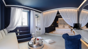 A modern hotel room with a large bed, a sofa, a round coffee table, and a blue armchair.