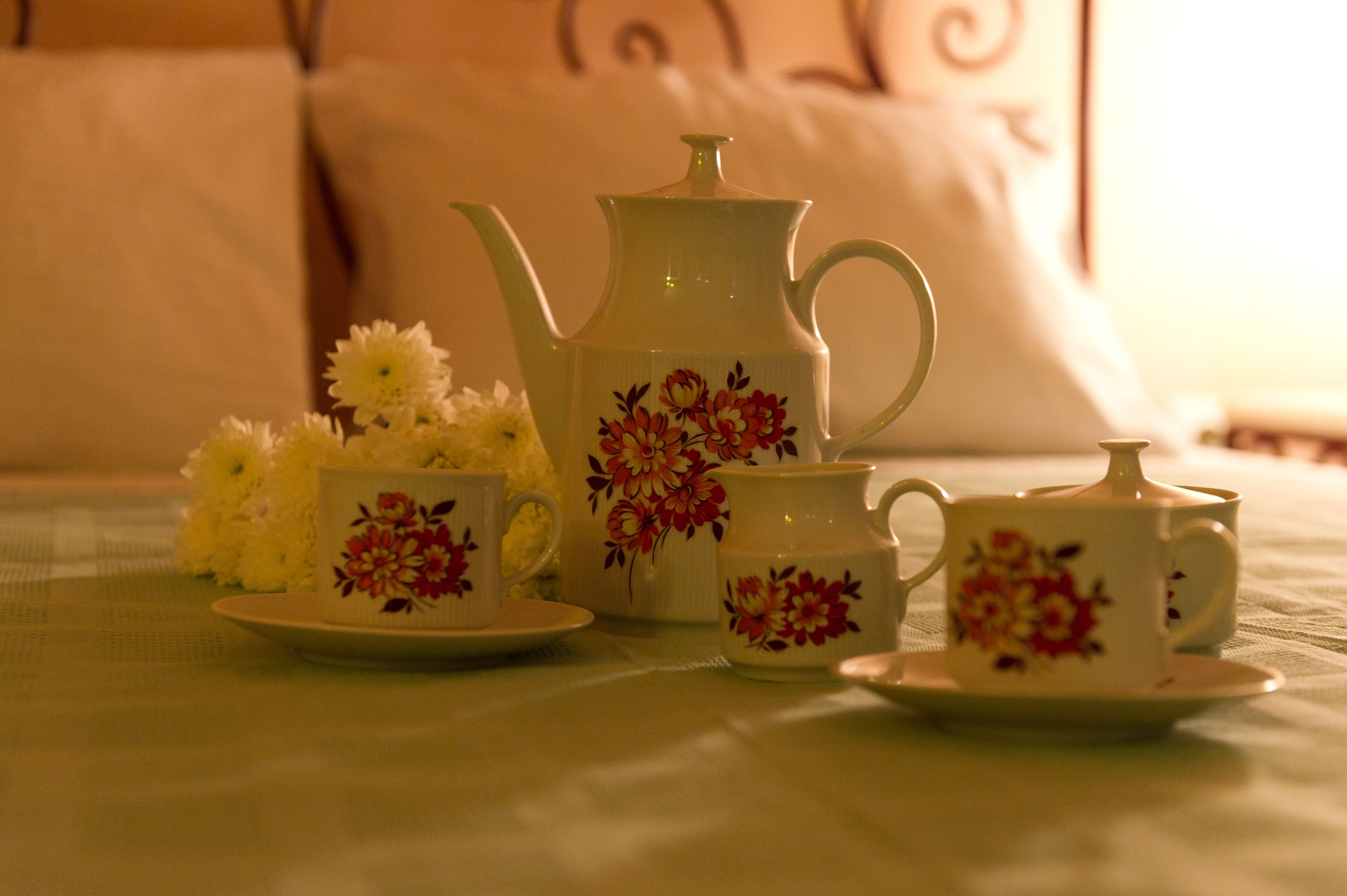 A tea set with floral designs on a tablecloth, accompanied by a bouquet of white flowers.