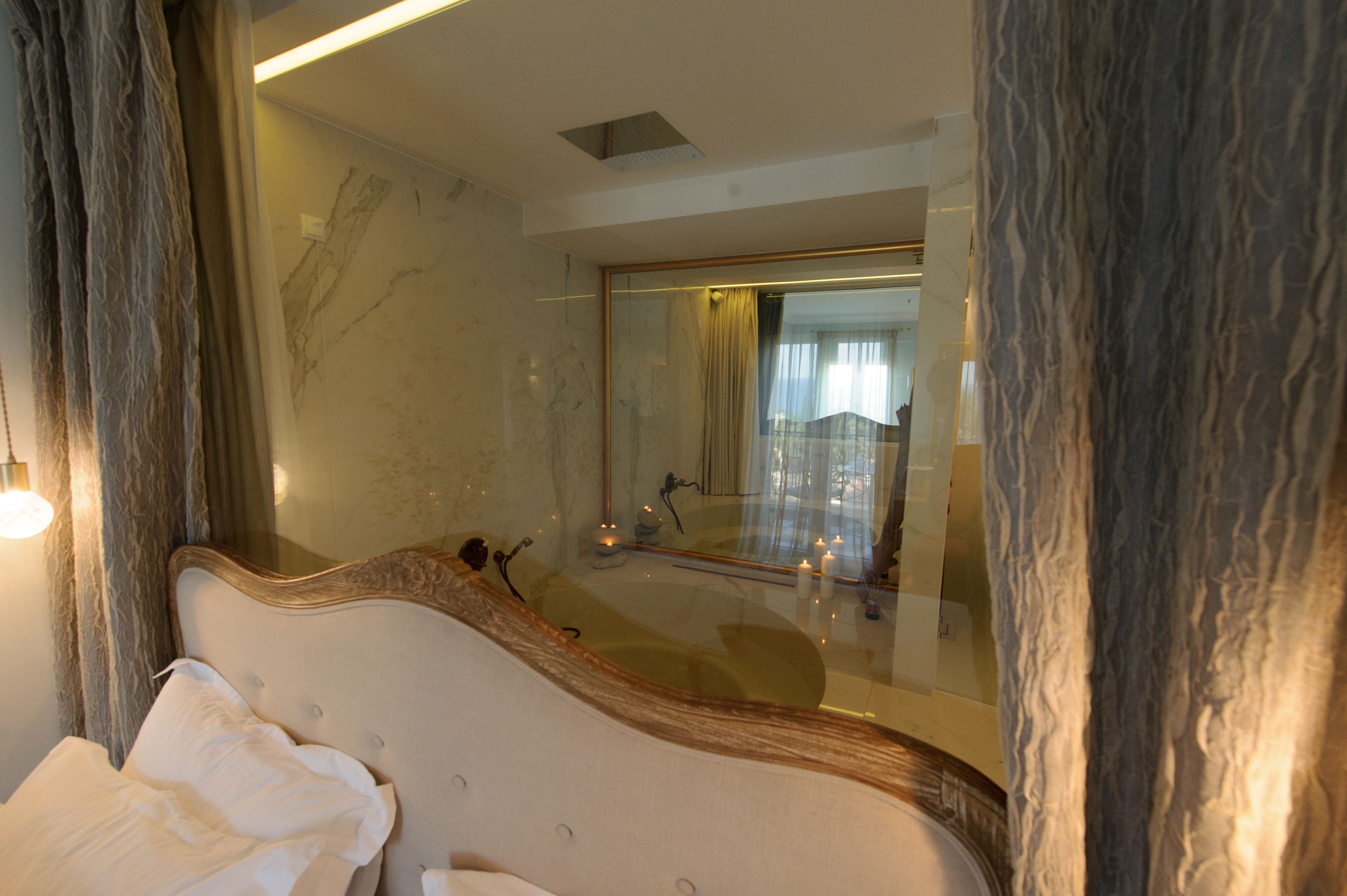 A bedroom with a large mirror, a bed with white linens, and a marble wall.