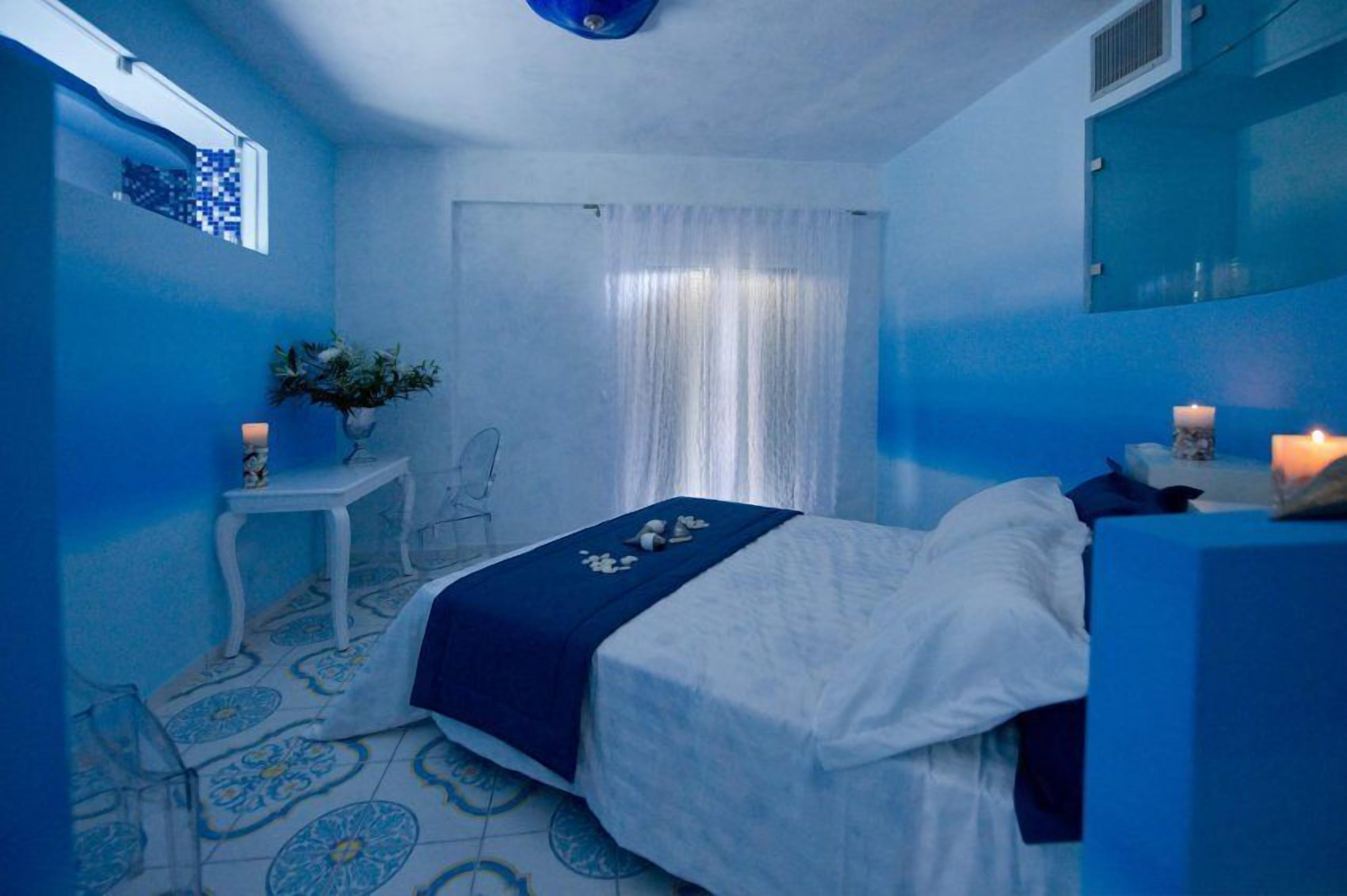 A bedroom with a bed, a small table with a vase, and a mirror.