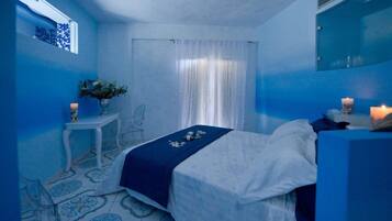 A bedroom with a bed, a small table with a vase, and a mirror.