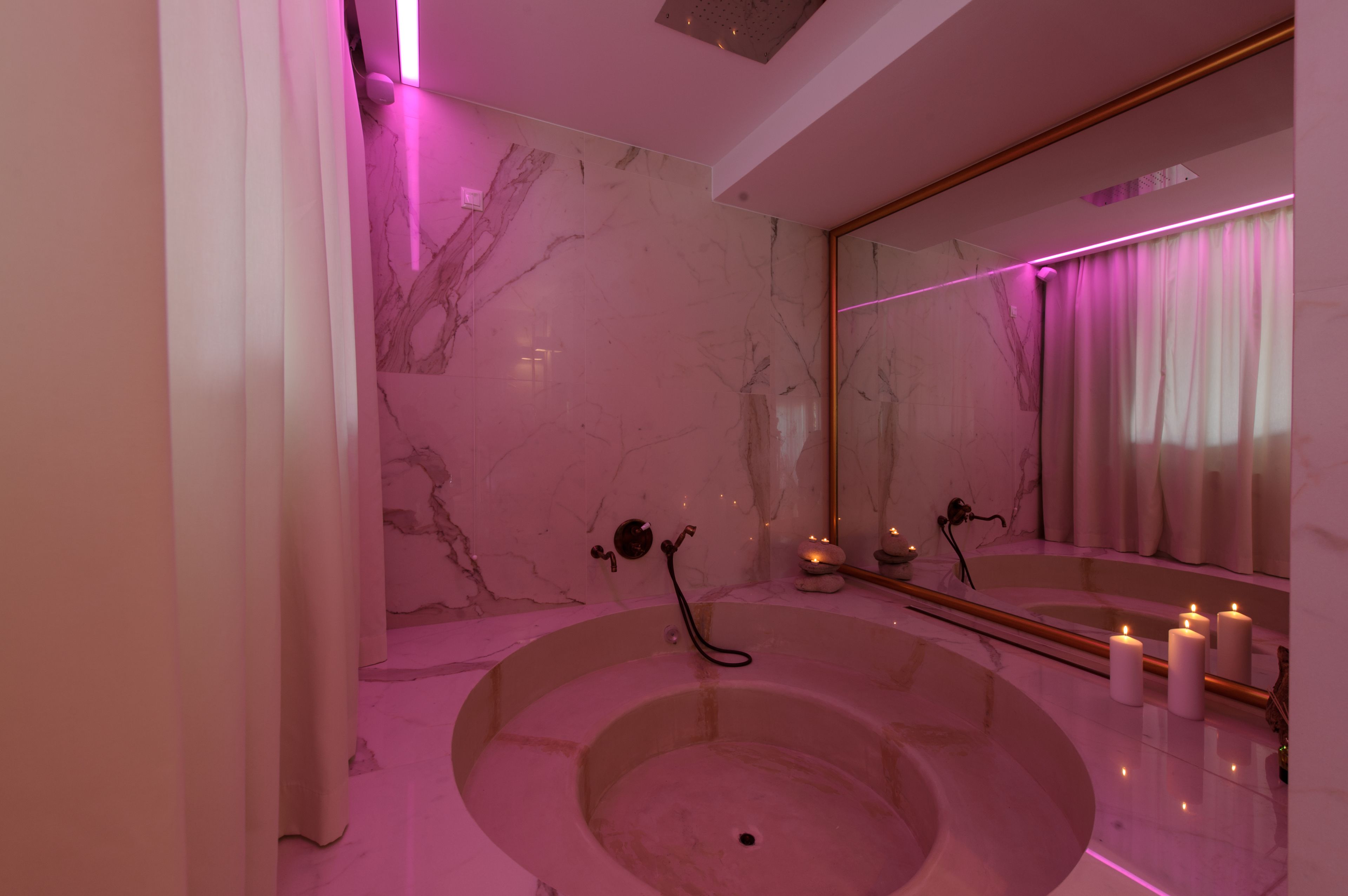 A modern bathroom with a marble wall, a large bathtub, and a mirror with a curtain.