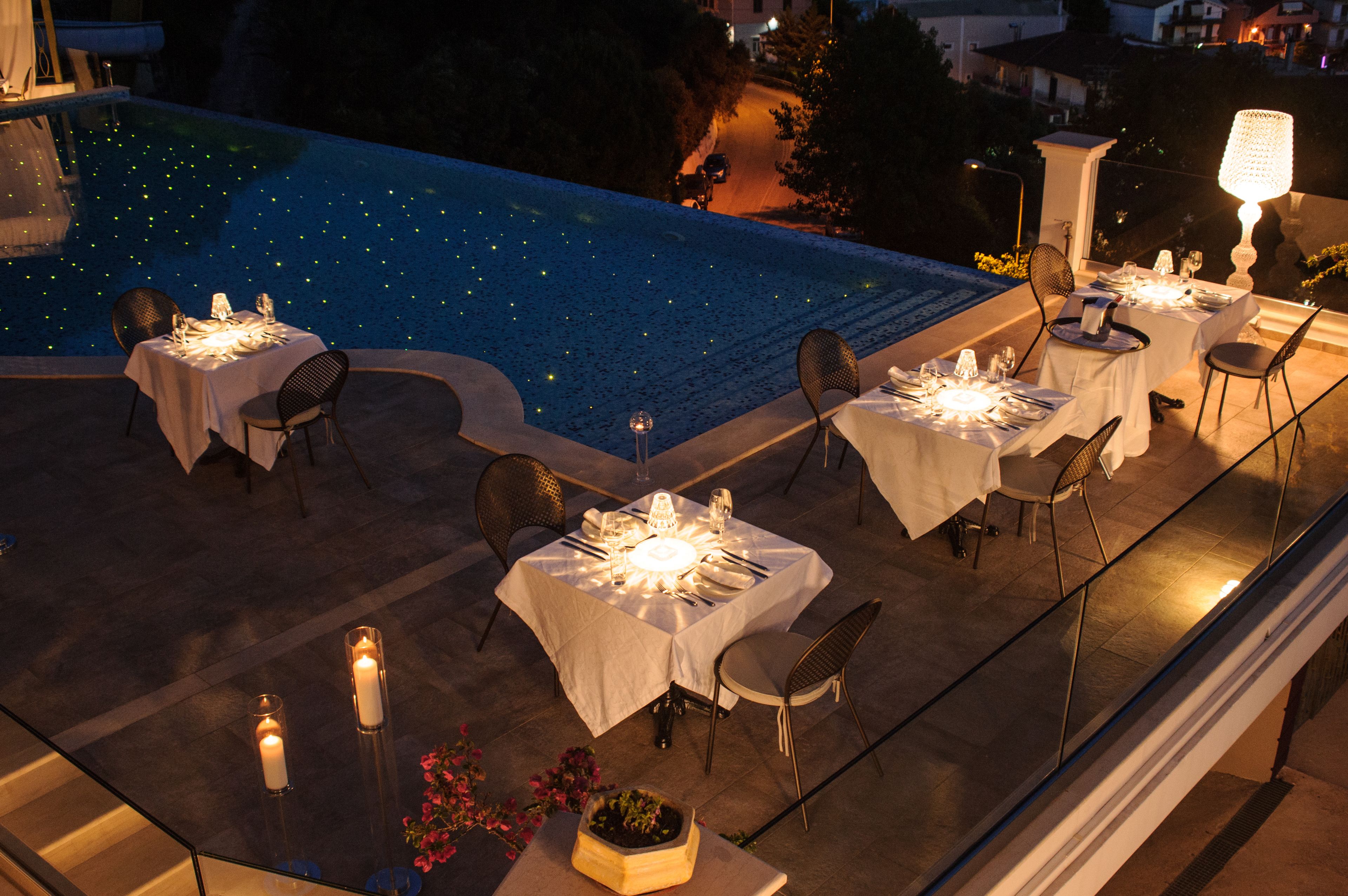 An outdoor dining area with tables set for two, overlooking a pool with star-shaped lights.