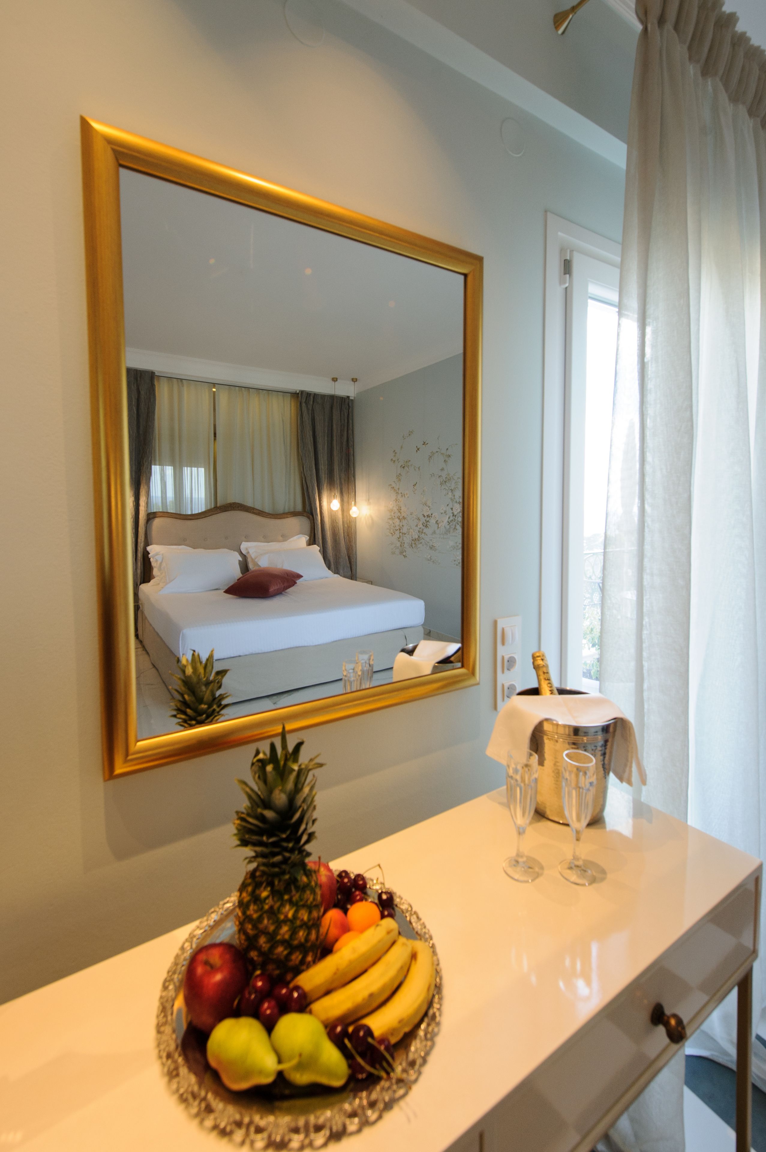 Een hotelkamer met een bed, een spiegel, een schaal fruit en een minibars.