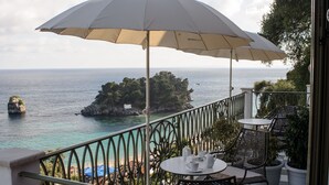 A balcony with a table and chairs, a white umbrella, and a view of the sea and a rocky island.