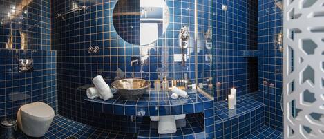 A bathroom with blue tiled walls, a round mirror, a sink with a bowl, and a toilet.