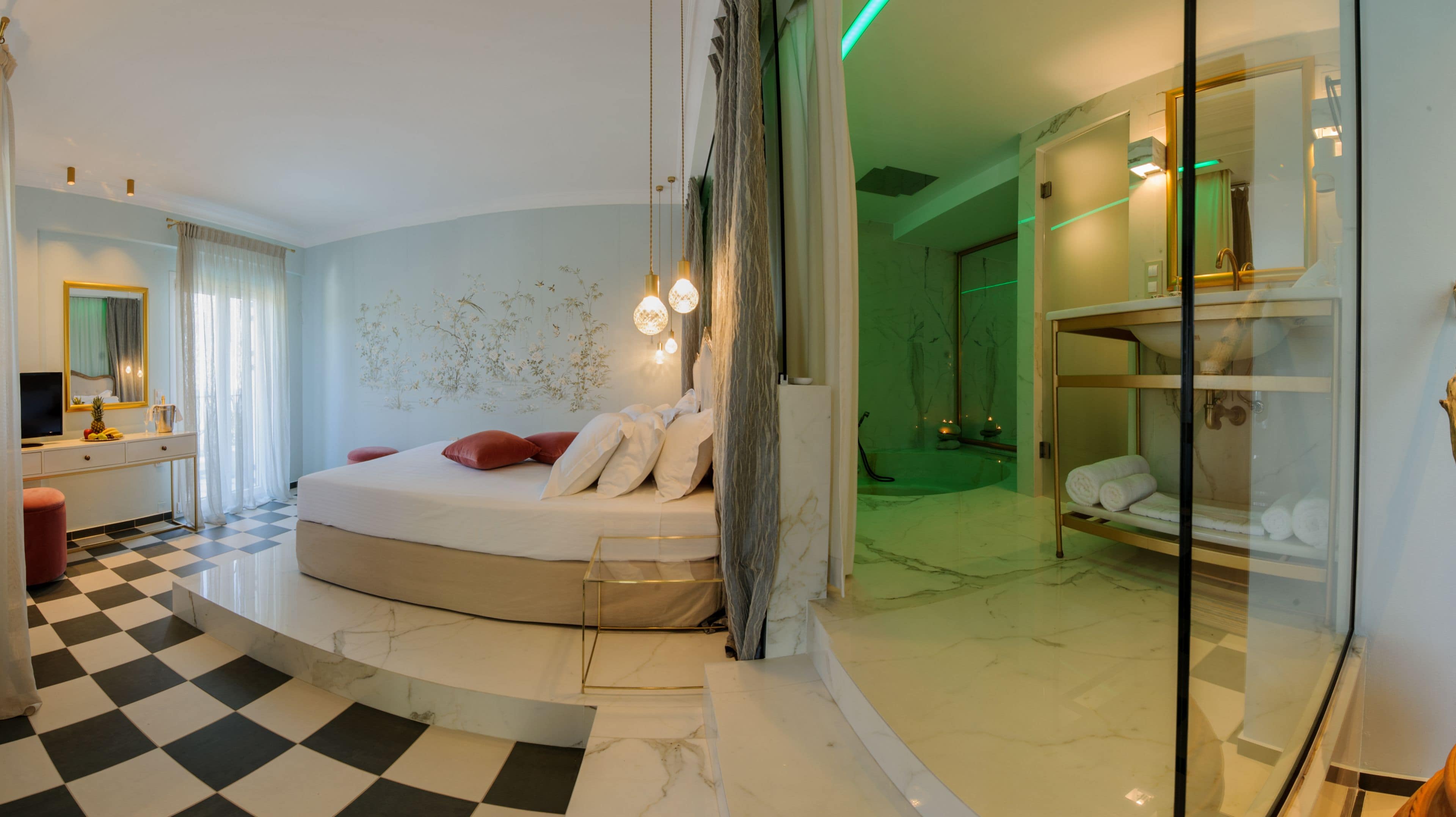 Un dormitorio moderno con una cama curvada, un tocador con espejo y un baño separado con cabina de ducha de vidrio.