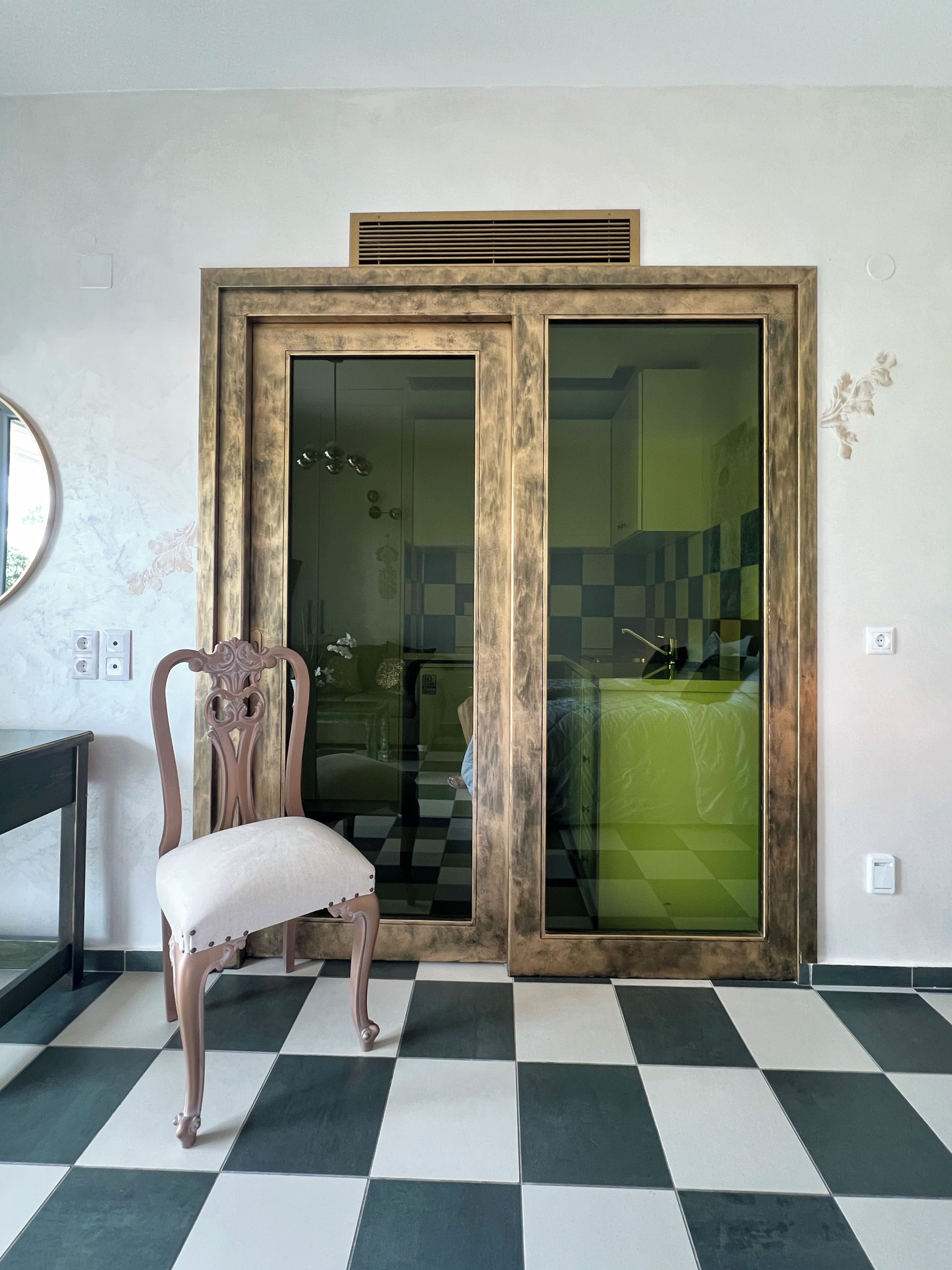Una habitación con piso de cuadros, una silla de madera y una puerta corrediza de vidrio que da a un baño.