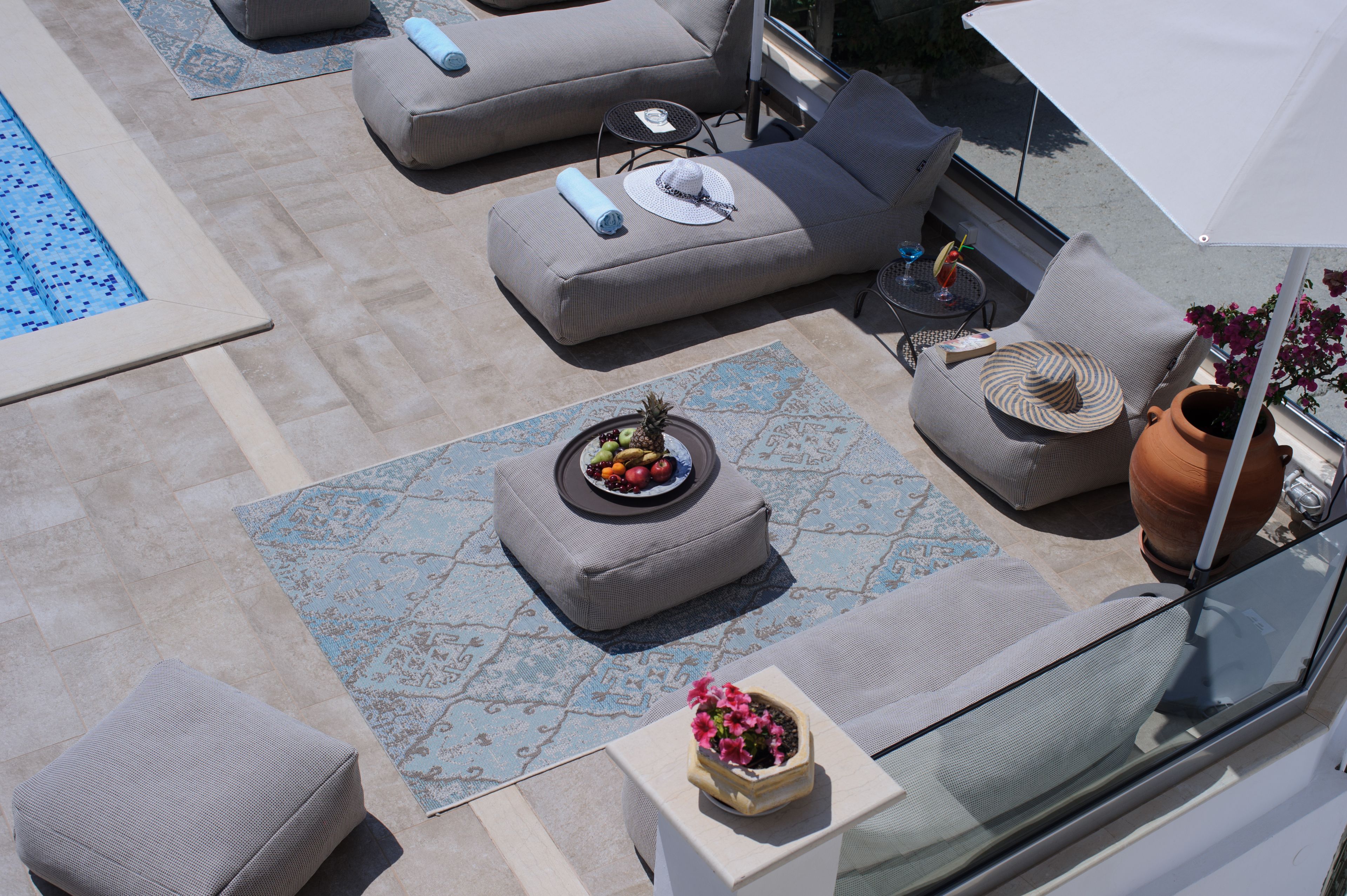 A rooftop terrace with a pool, lounge chairs, a table with drinks, and a potted plant.