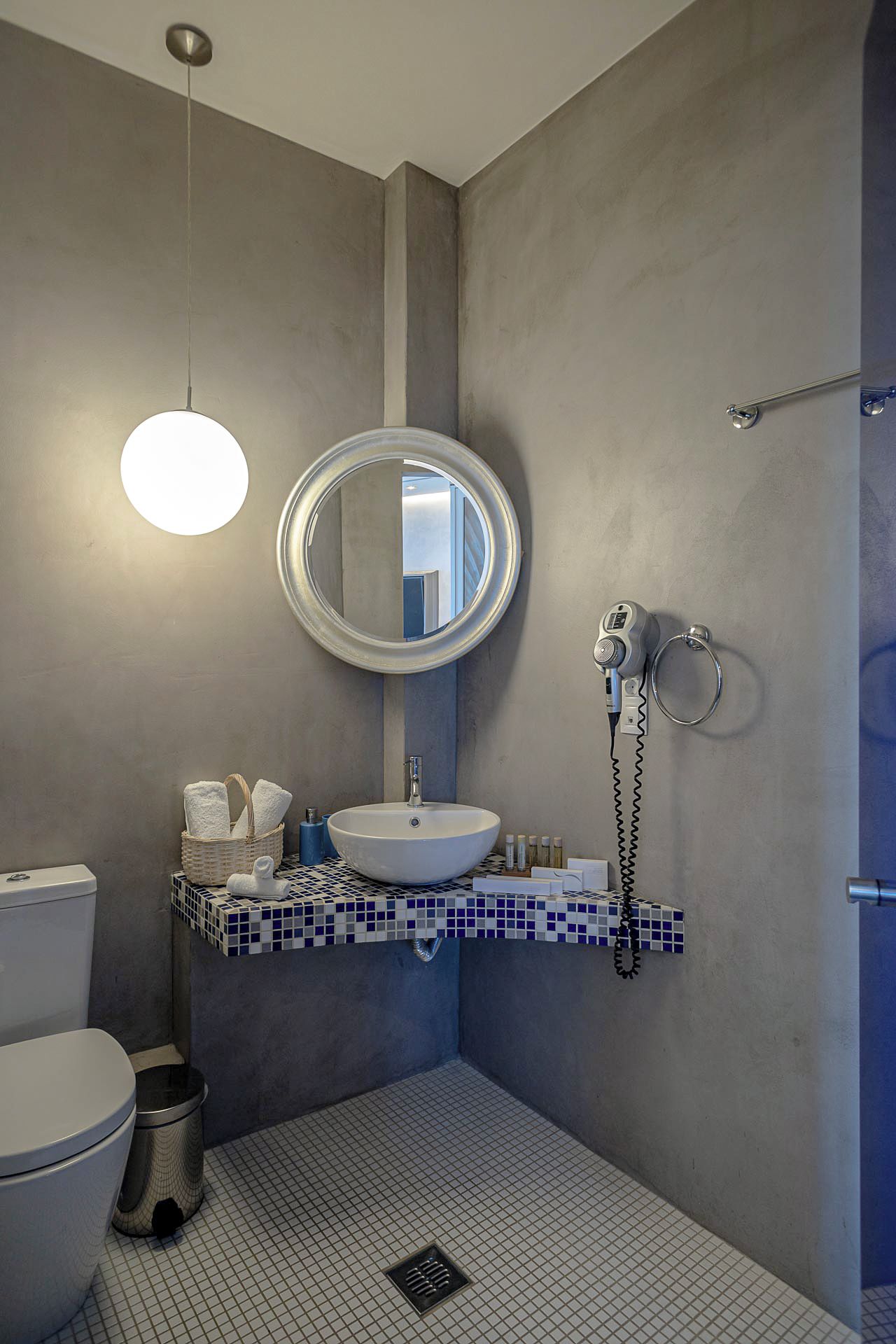 A bathroom with a white sink, a round mirror, a hairdryer, and a towel rack.