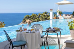 A poolside dining area with a table set for two, overlooking a clear blue sea and lush greenery. - Irida Parga (Parga)