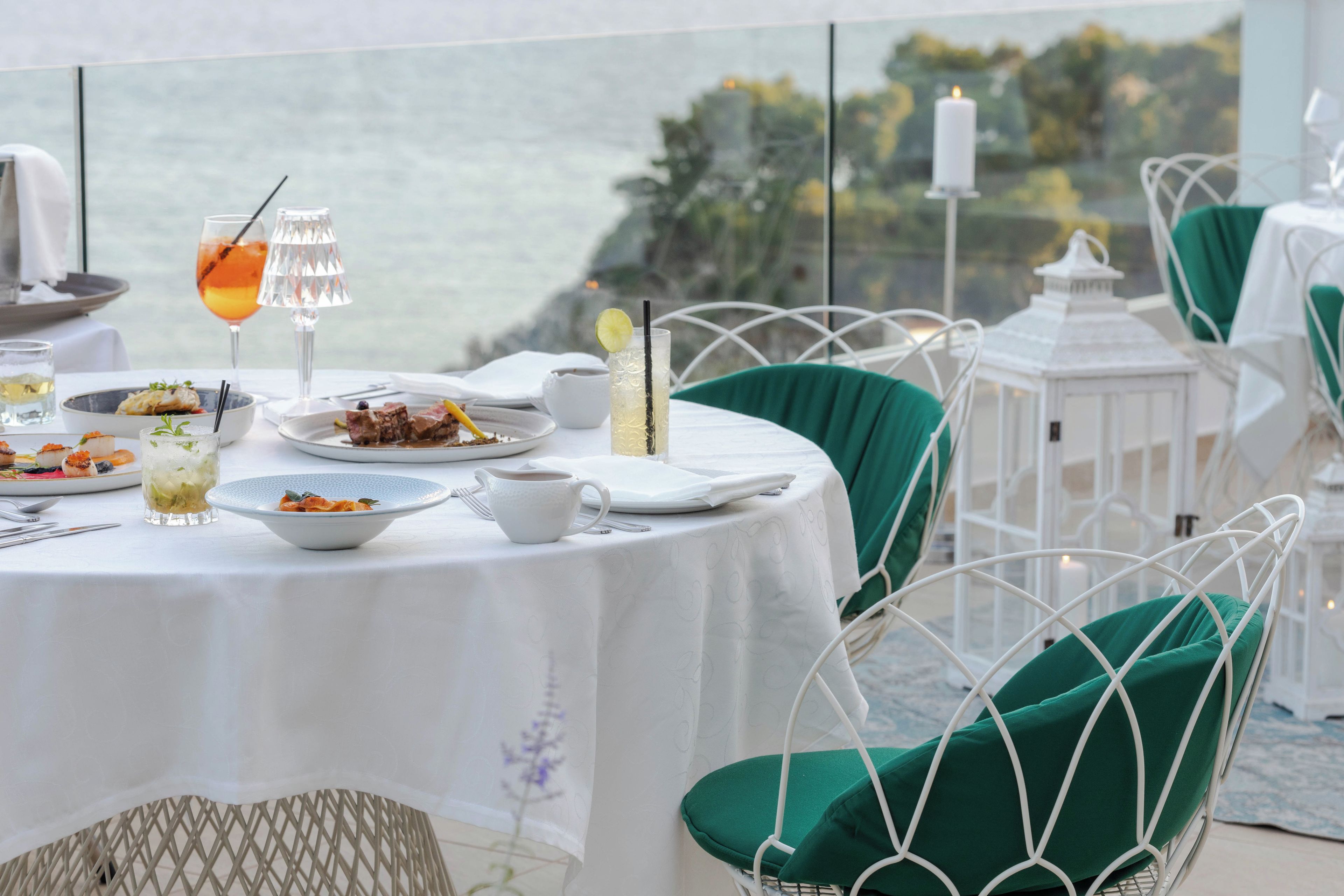 Mesa lista con platos, vasos y una vela, con vistas a un paisaje pintoresco.