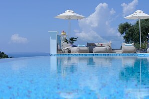 A clear blue pool with lounge chairs and umbrellas, a decorative fountain, and a view of the sea. - Irida Parga (Parga)