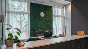 Een receptiebalie met een groene muur, een klok en een bord met daarop de in- en uitchecktijden en openingstijden voor ontbijt.