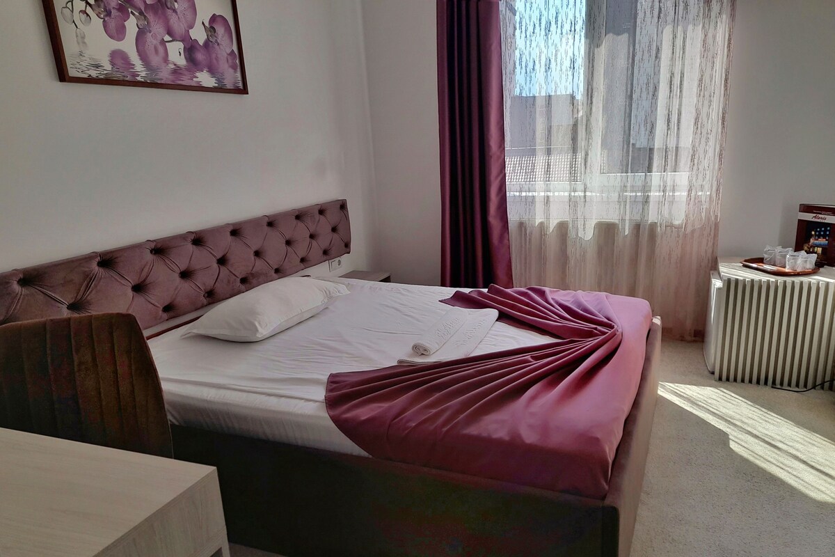 A neatly made bed with a tufted headboard, a bedside table, and a radiator.