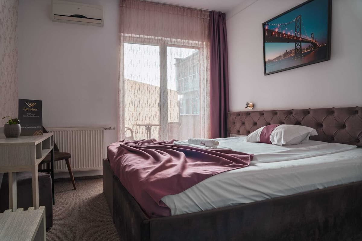 A hotel room with a bed, a desk, and a window with curtains.