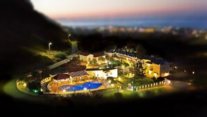 Un complejo turístico frente al mar con piscina, varias edificaciones y un paseo marítimo bien iluminado.