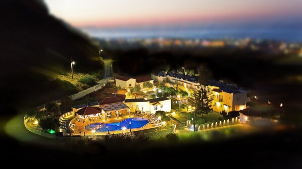 Un complejo turístico frente al mar con piscina, varias edificaciones y un paseo marítimo bien iluminado.