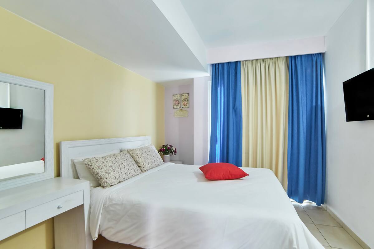 Una habitación de hotel con una cama, una mesita de noche, un televisor y cortinas.