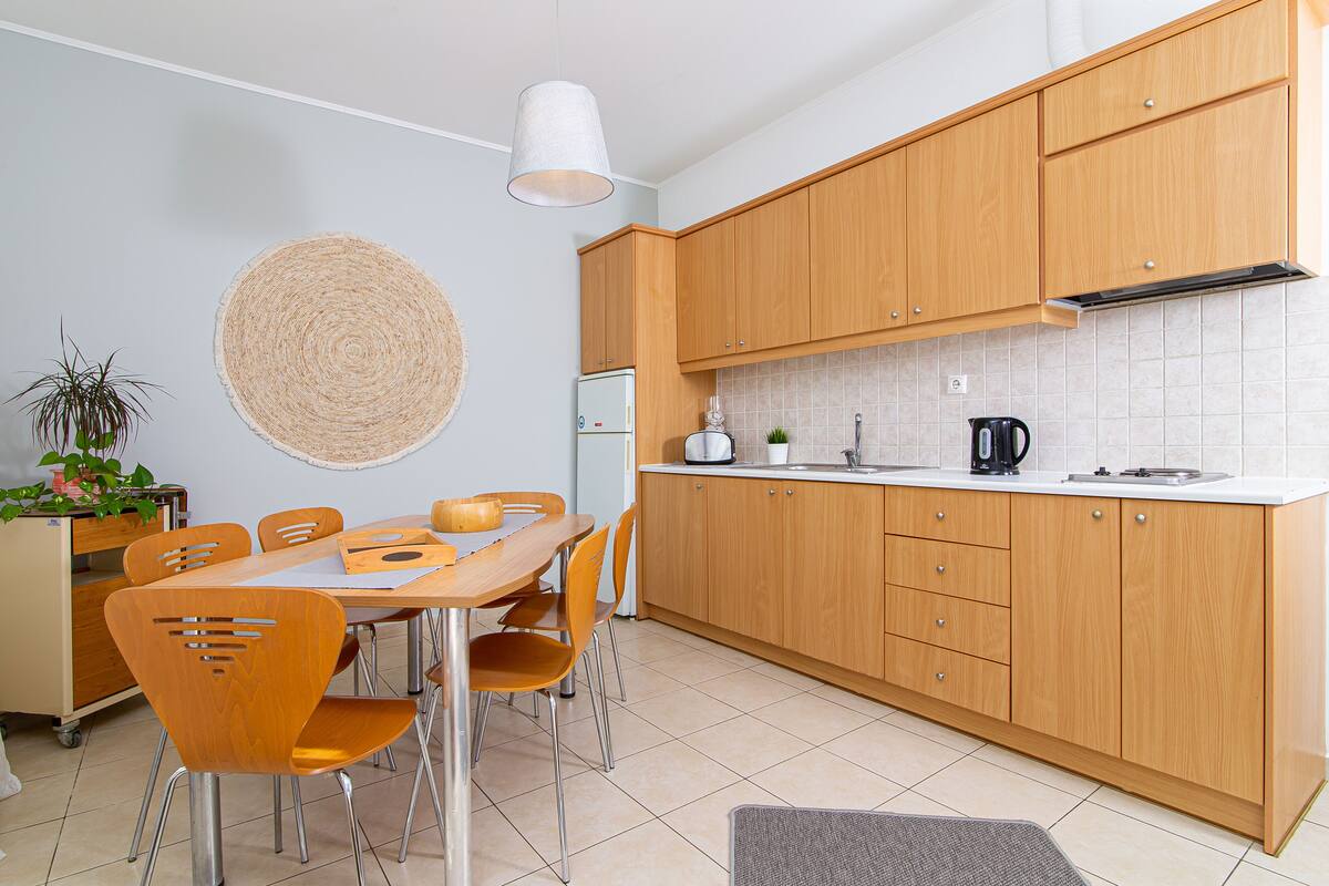 Una cocina moderna con armarios de madera, una mesa de comedor con sillas y una isla de cocina con un lavamanos y un hervidor.