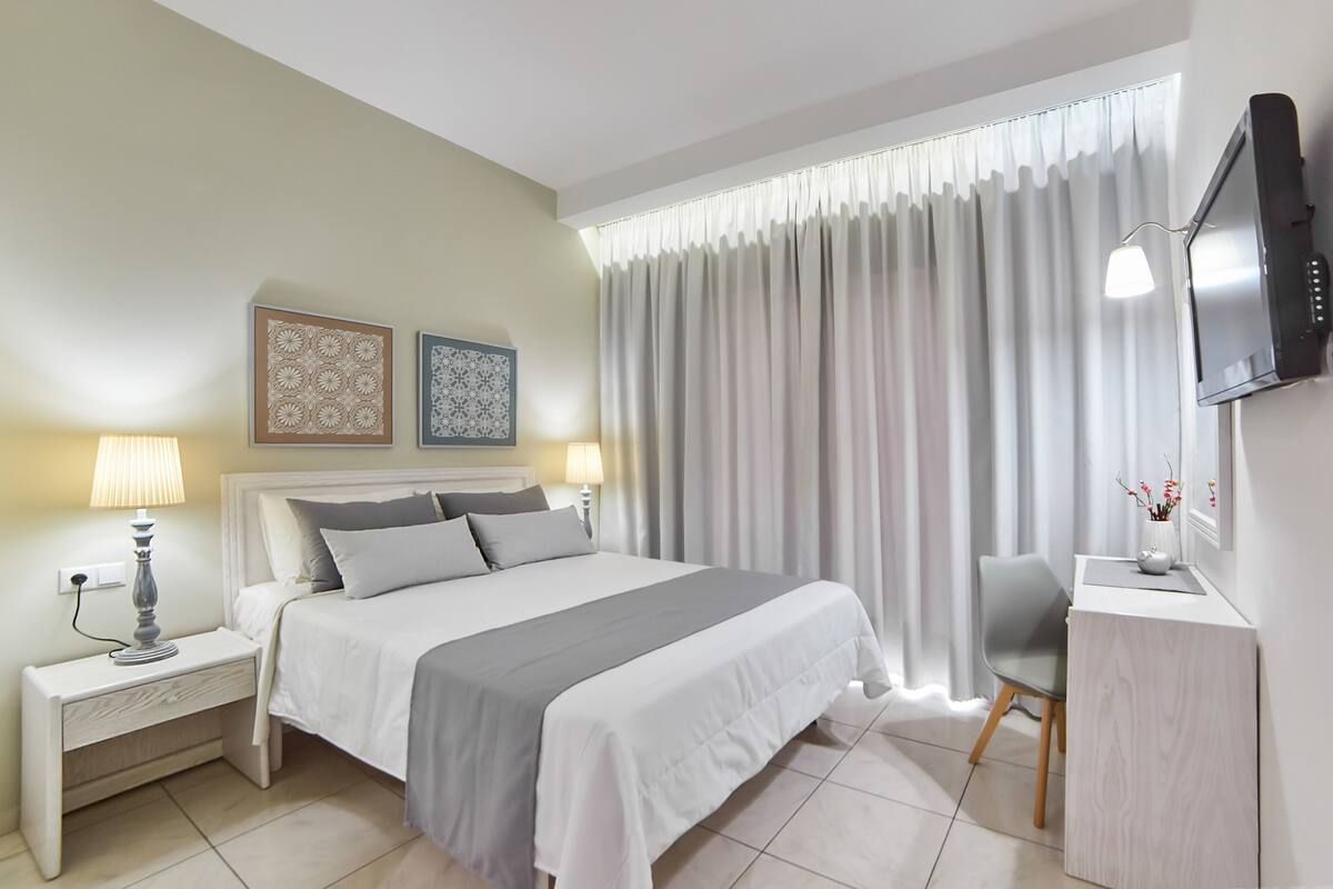Un dormitorio ordenado con cama, mesitas de noche, escritorio y televisor.