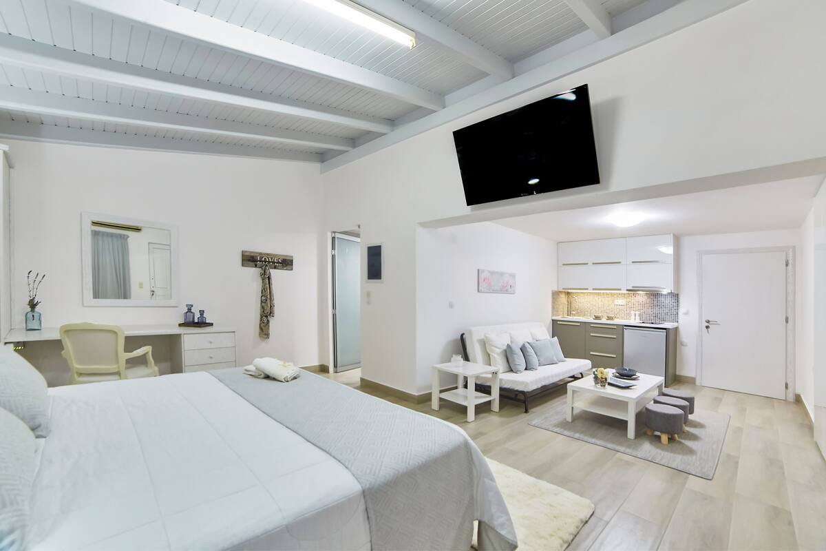 Una habitación de hotel moderna con una cama grande, un escritorio, un sofá, un televisor y una kitchenette.