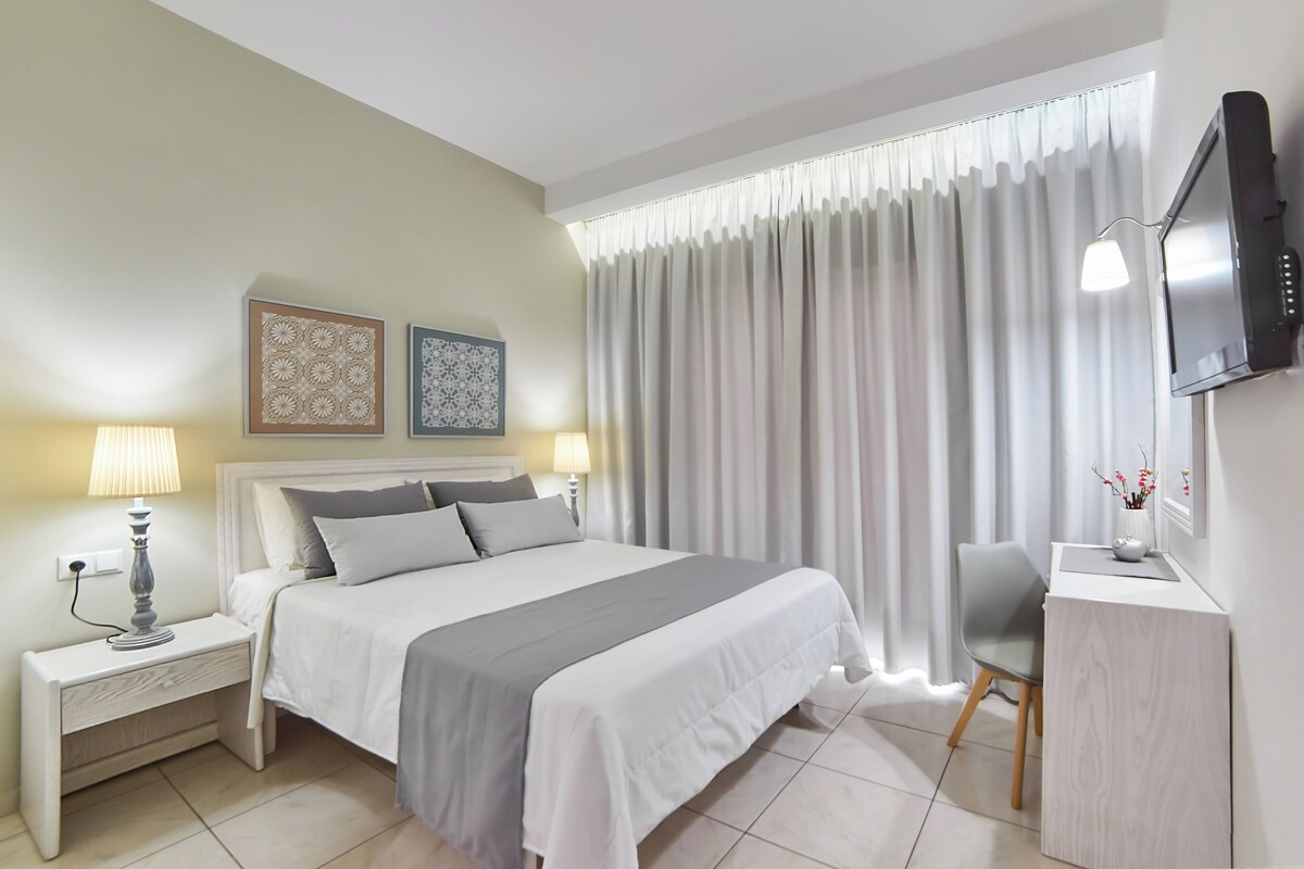 A neatly arranged bedroom with a bed, bedside tables, a desk, and a TV.