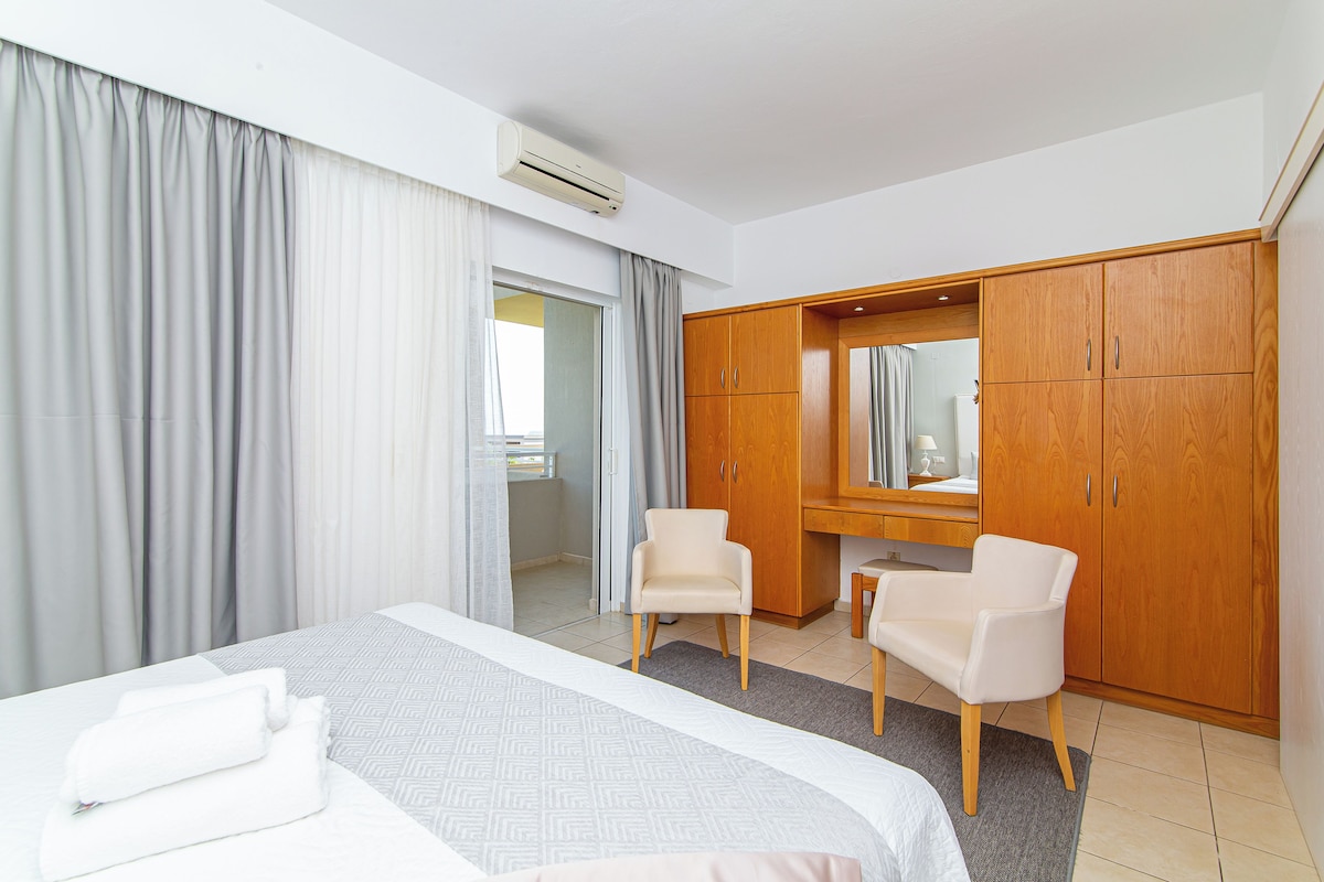 A hotel room with a bed, two chairs, a wardrobe, and a mirror.