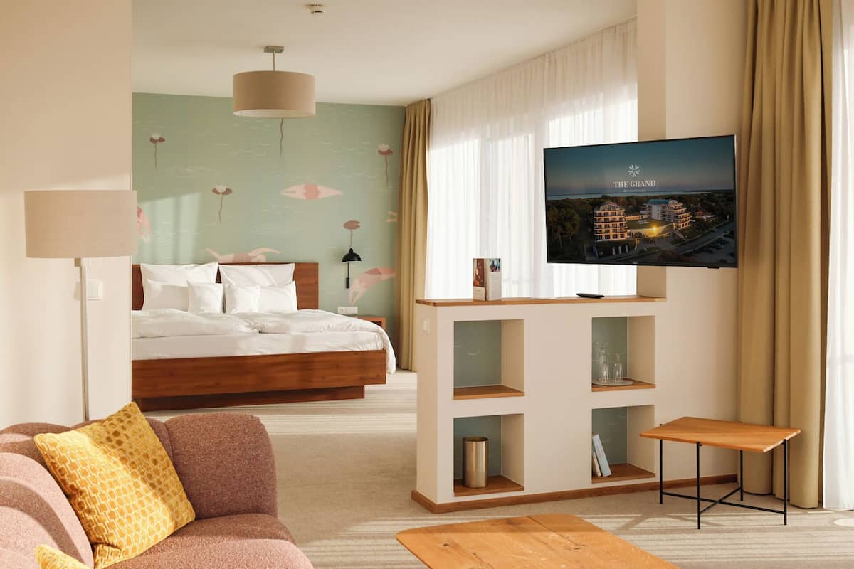A hotel room with a bed, a TV mounted on a wall, a sofa, a coffee table, and a decorative wall with a cityscape view.