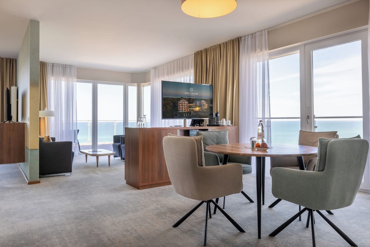A hotel room with a dining area, a TV, and a view of the ocean.