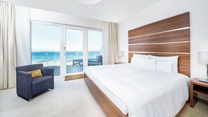 A hotel room with a large bed, a sofa, a nightstand, and a view of the ocean through a sliding door. - THE GRAND Ahrenshoop (Ostseebad Ahrenshoop)