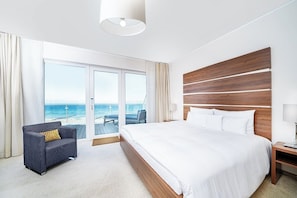 Ett hotellrum med en stor säng, en soffa, ett nattduksbord och utsikt över havet genom en skjutdörr.