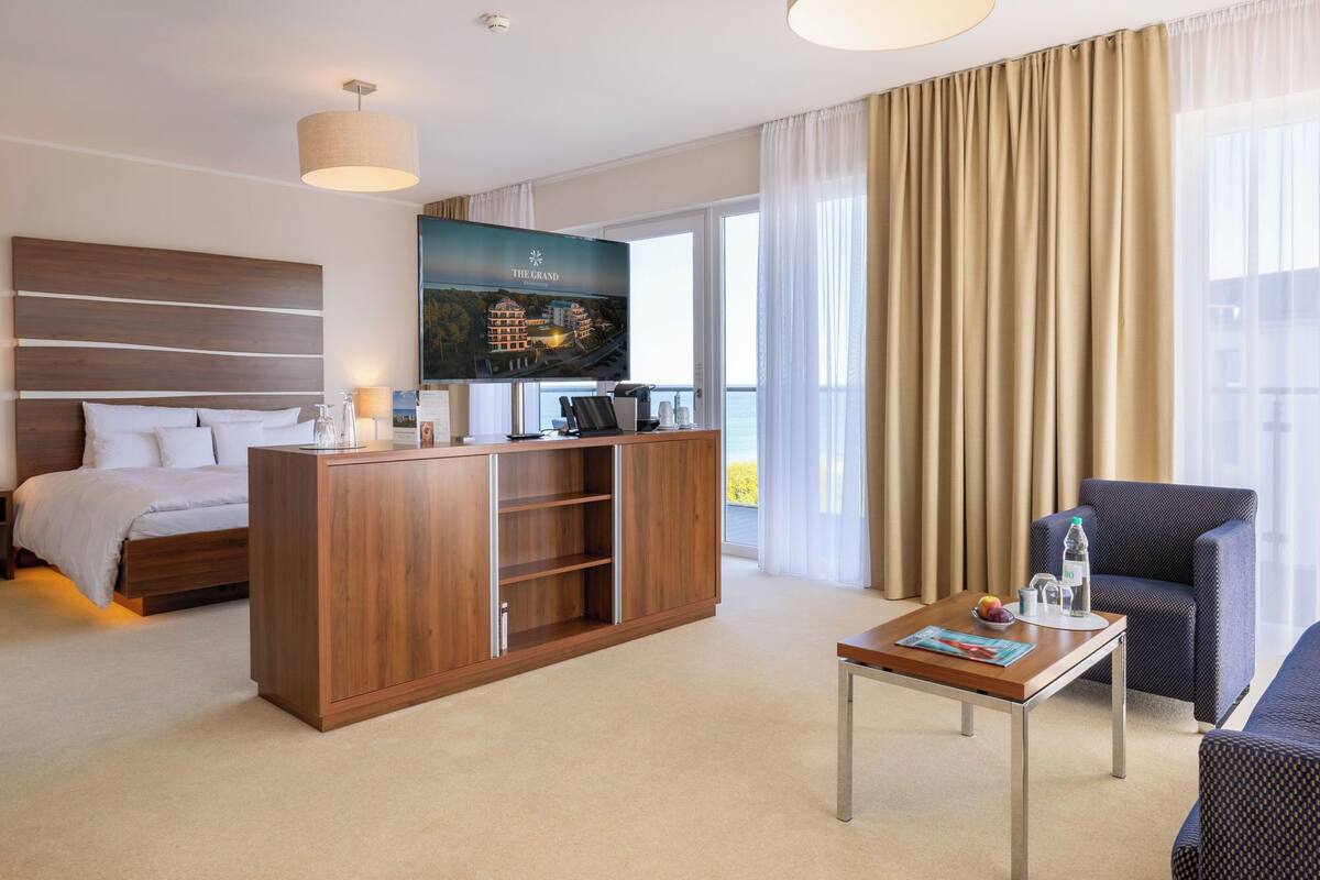 A hotel room with a bed, a wooden desk, a television, and a view of the sea.