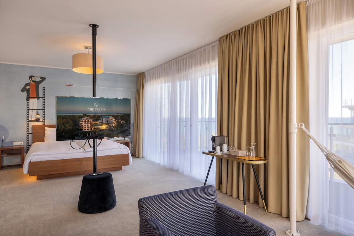 A hotel room with a bed, a TV mounted on the wall, a small table with a coffee maker, and a window with curtains.