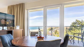 A hotel room with a balcony, a dining table with chairs, a TV, and a bottle of water.