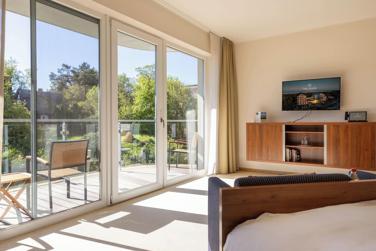 A hotel room with a bed, a TV mounted on the wall, a wooden cabinet, and a sliding glass door leading to a balcony.