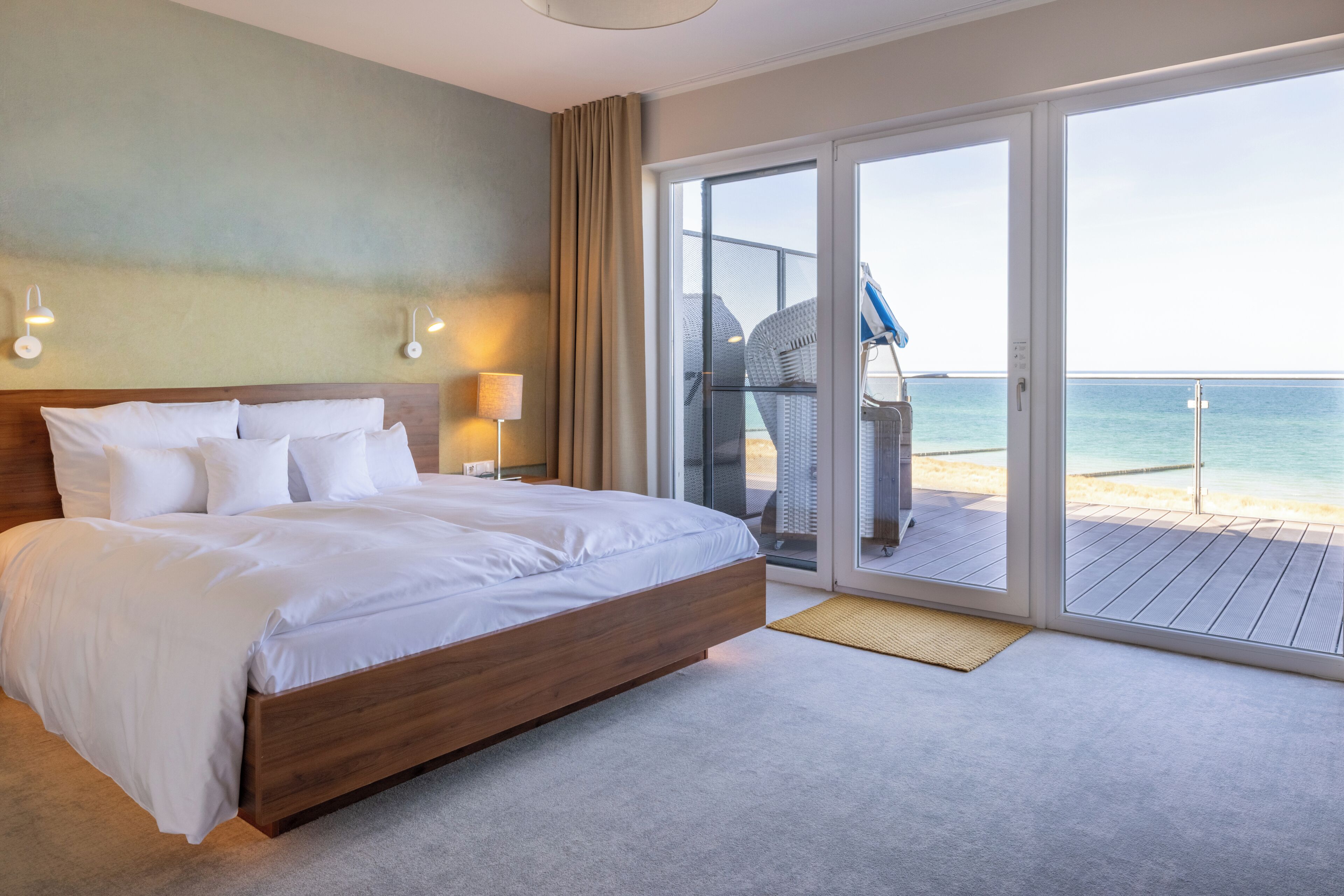 A hotel room with a large bed, a balcony with a view of the sea, and a chair.