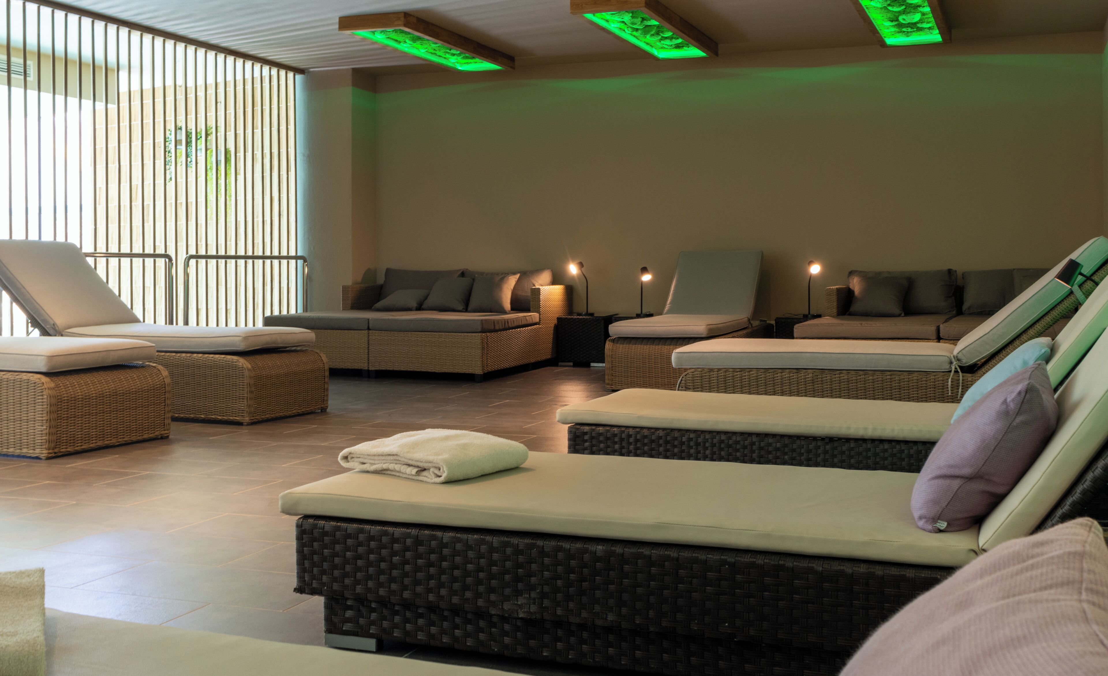 Un cuarto de spa con varias sillas reclinables, un ventanal con persianas verticales e iluminación ambiental verde.