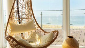 A wicker hanging chair with cushions and a vase on a balcony with a view of the sea. - THE GRAND Ahrenshoop (Ostseebad Ahrenshoop)