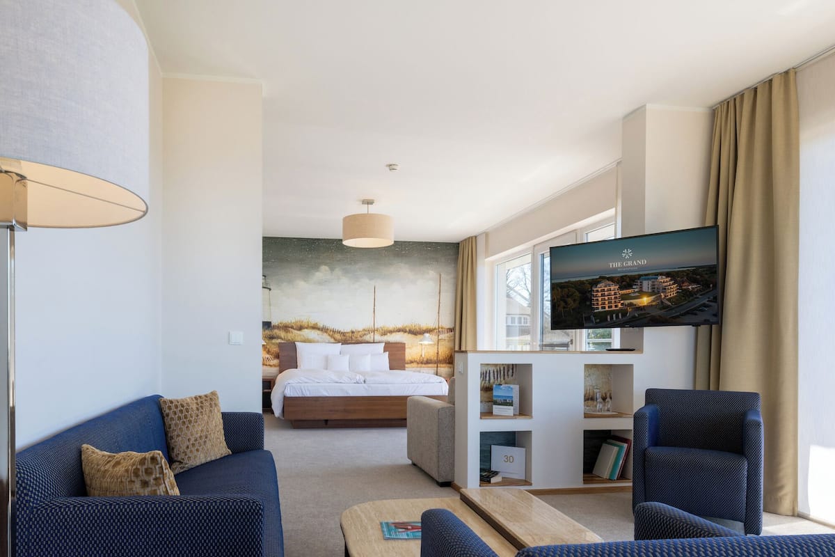 A hotel room with a bed, a TV, a sofa, and a bookshelf.