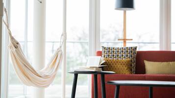Et værelse med hængekøje, rød sofa, mønstret pude, lampe og et lille bord med en bog.