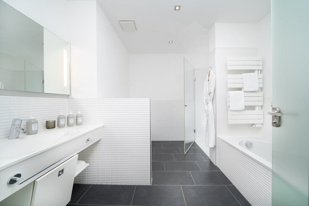 Une salle de bain moderne avec un meuble-lavabo blanc, un grand miroir, une douche en verre et une baignoire blanche.