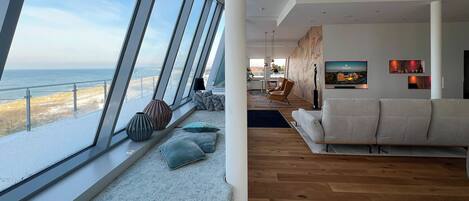 Un salon moderne avec une grande fenêtre donnant sur une plage enneigée, un canapé et un téléviseur fixé au mur.