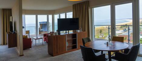 Una habitación amplia con un ventanal grande, un televisor de pantalla plana, un mueble de madera y una mesa de comedor redonda con sillas.