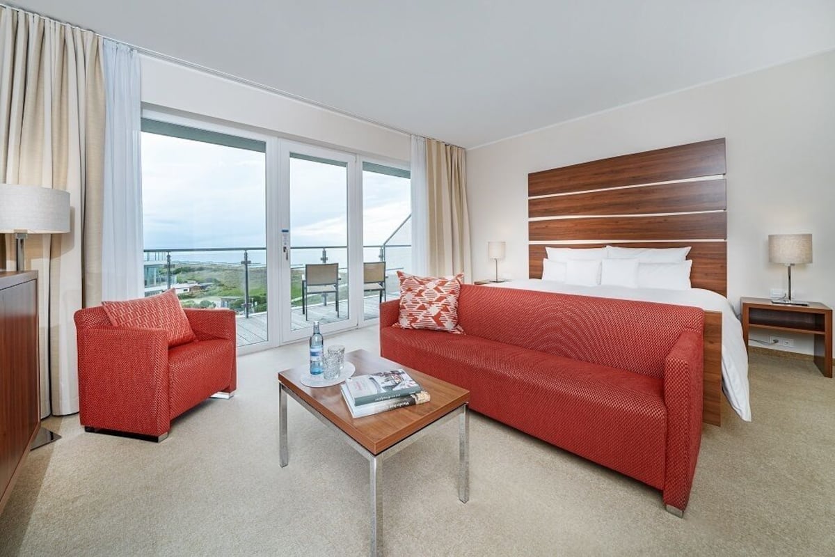 A hotel room with a large bed, a red sofa, a coffee table, and a balcony with a view.