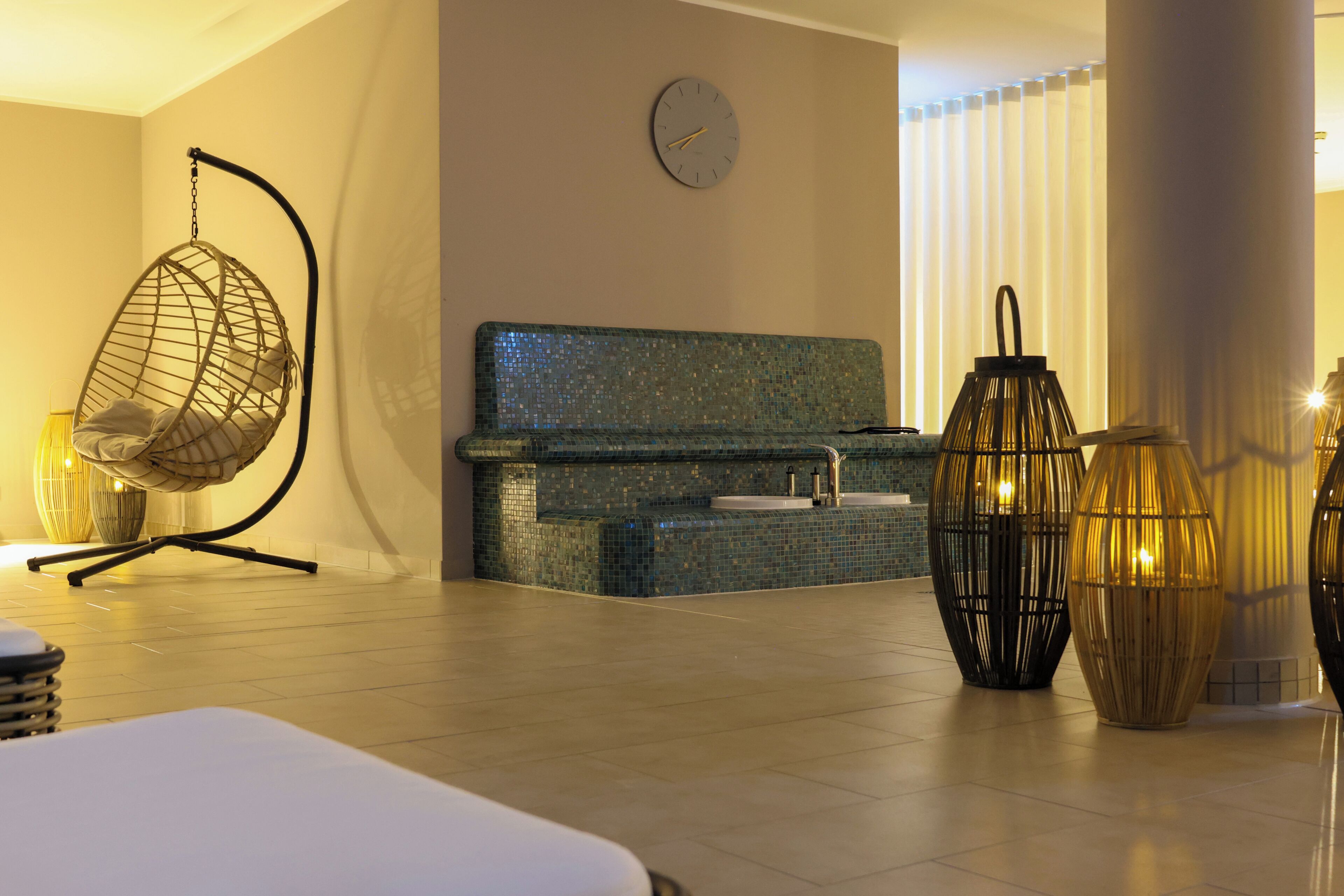 A modern spa room with a hanging chair, a massage table, a small sink, and decorative lanterns.
