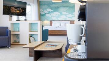 A hotel room with a bed, a TV, a coffee machine, a desk, and a wall with a fish pattern.